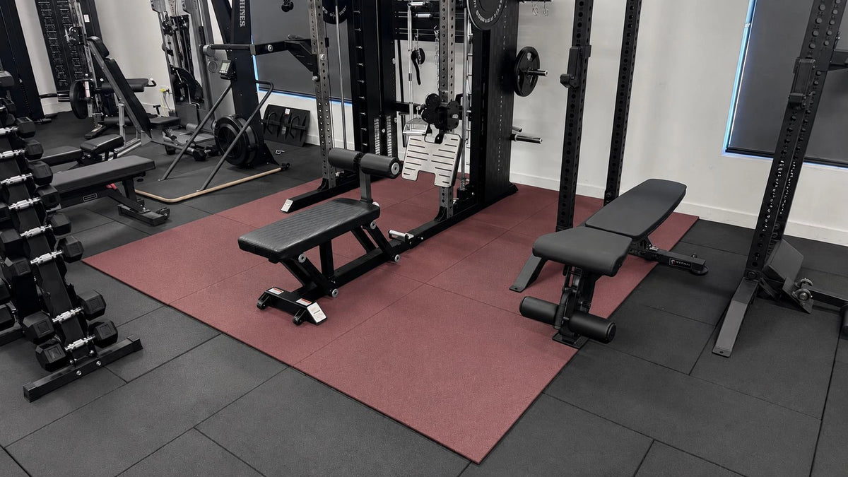 Red rubber gym flooring tiles installed in a home gym with commercial fitness equipment