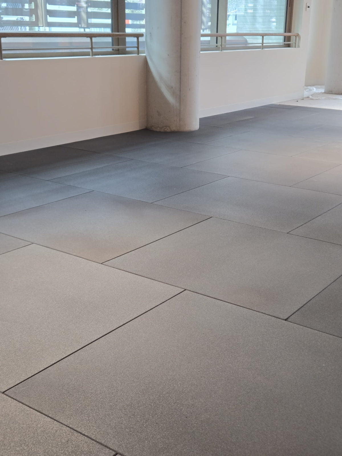 Large square gray floor tiles installed in a modern indoor space with white walls and windows.
