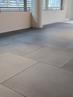 Large square gray floor tiles installed in a modern indoor space with white walls and windows.
